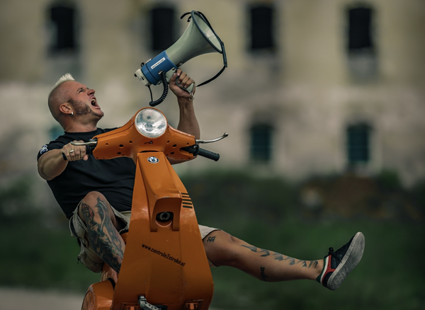 Stuntman Wheelies Vespa einen Berg hinauf, während er die Augen verbundene