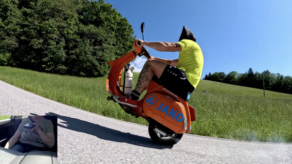 Stuntman Wheelies Vespa einen Berg hinauf, während er die Augen verbundene