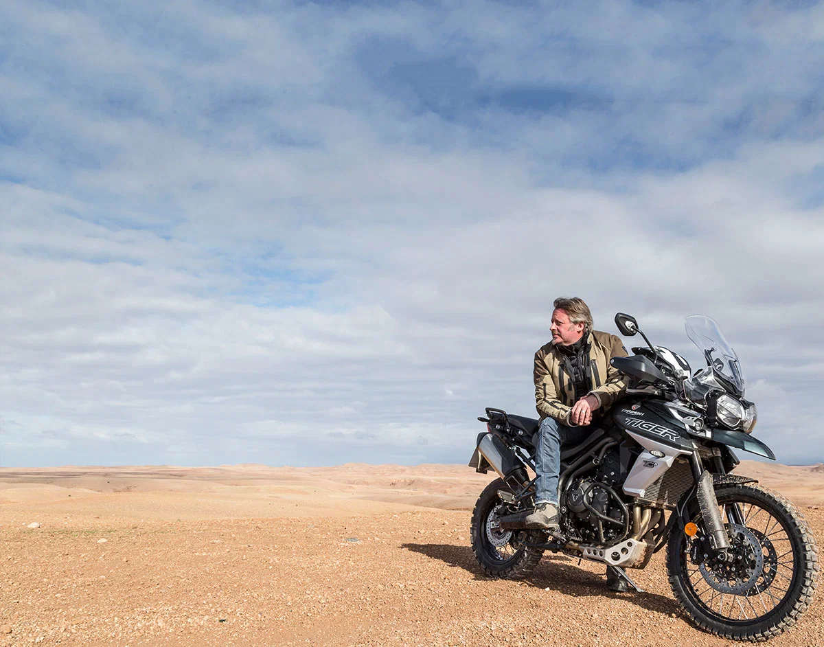 Charley Boorman sitzt auf einem Triumph Tiger-Fahrrad.