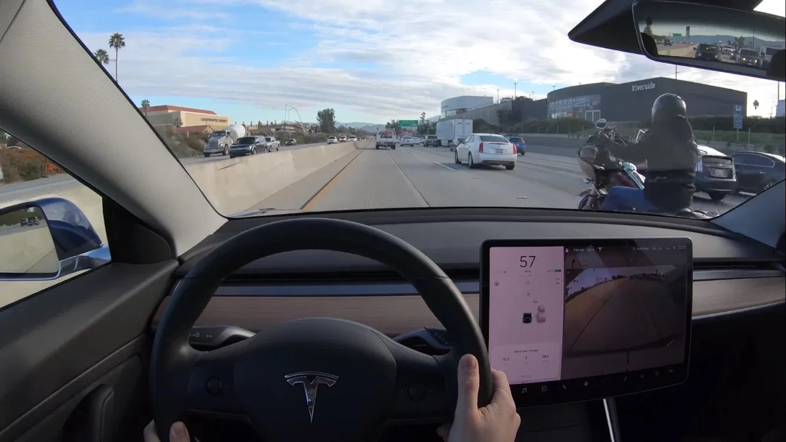 Ein Tesla fährt auf der Autobahn, rechts daneben ein Motorrad.